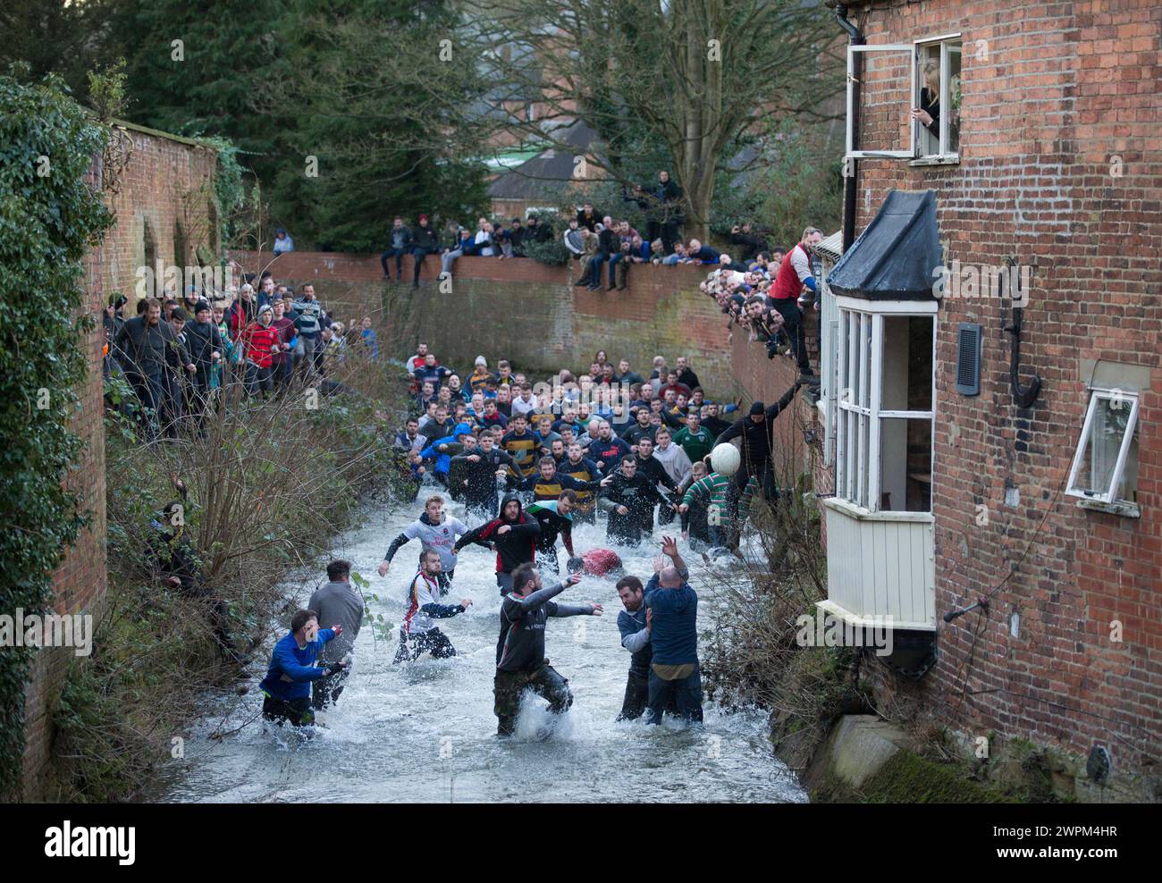 02/16 Spieler jagen den Ball durch Henmore Brook, während das Royal Shrovetide Football Match durch die Stadt Ashbourne in Derbyshire ausgetragen wird. U' Stockfoto