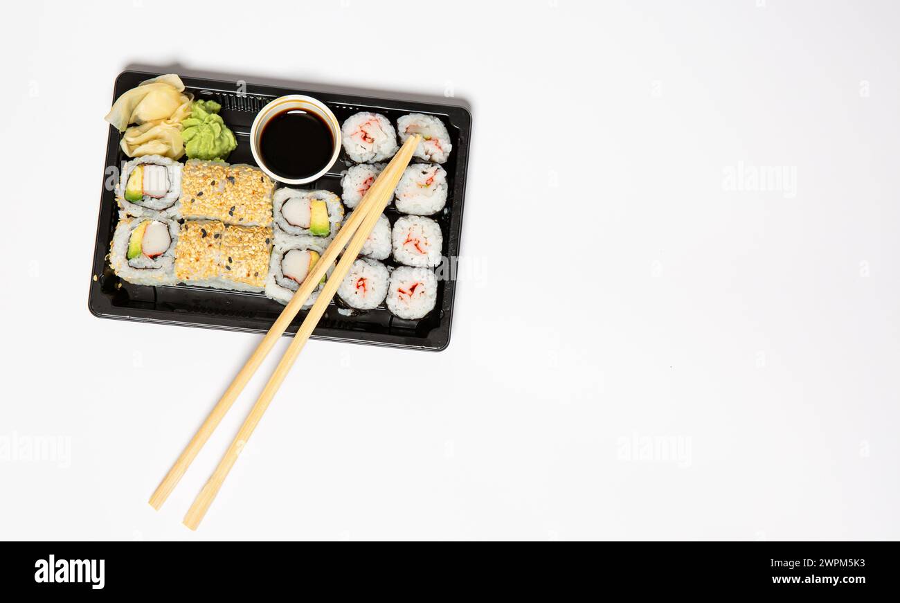 Sushi zum Mitnehmen in einer schwarzen Kiste mit Holzstäbchen auf weißem Hintergrund Stockfoto