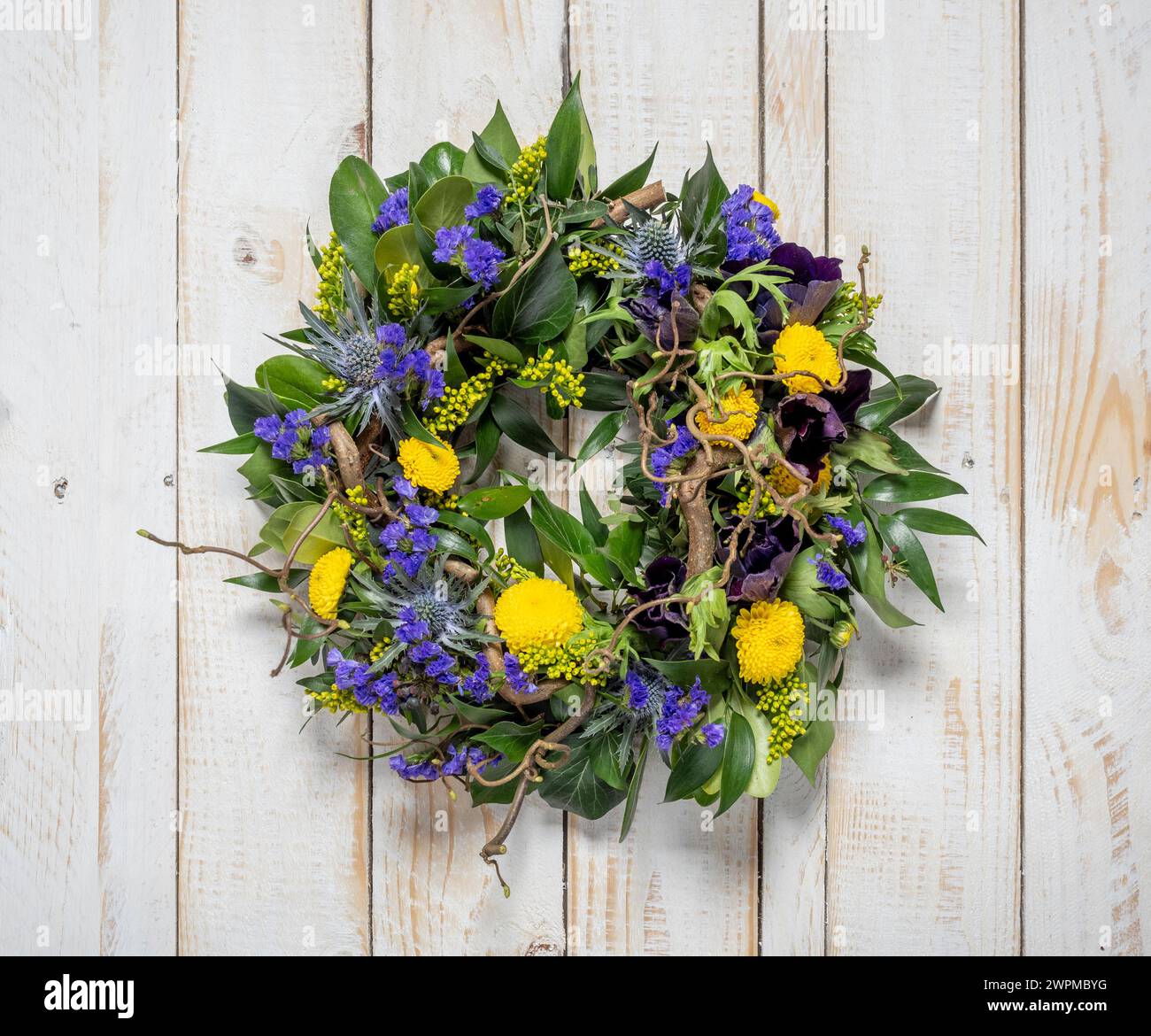 Frühlingskranz aus violetten und gelben Blumen auf einem rustikalen hölzernen, weiß getünchten Hintergrund Stockfoto