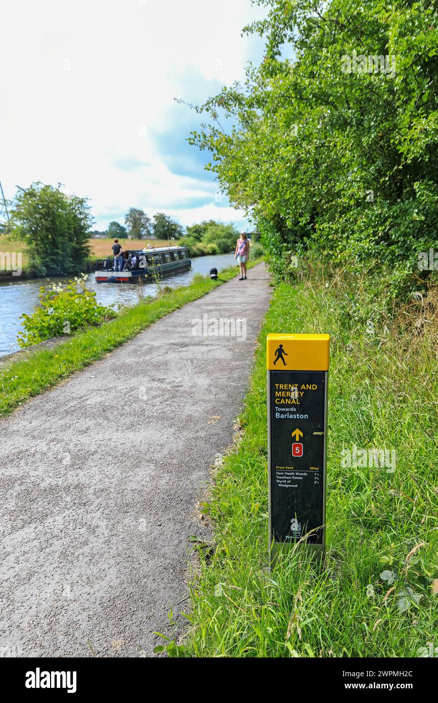 Ein Informationsschild oder ein Wegweiser auf dem Trent and Mersey Canal, mit einer Frau, die ihren Hund begleitet, Barlaston, Stoke on Trent, Staffordshire, England, UK Stockfoto