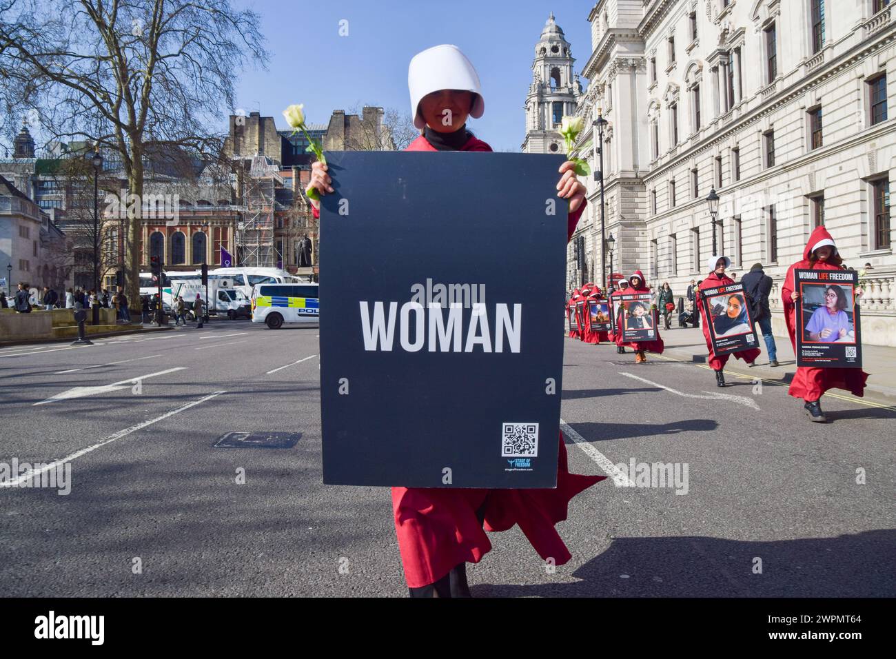 London, Großbritannien. März 2024. Während der Demonstration marschiert ein Demonstrant auf dem Parlamentsplatz mit einem „Frauen“-Plakat. Frauen in den Kostümen der Magd's Tale zogen am Internationalen Frauentag durch die Londoner Innenstadt, um die Freiheit des Iran zu unterstützen. Quelle: SOPA Images Limited/Alamy Live News Stockfoto