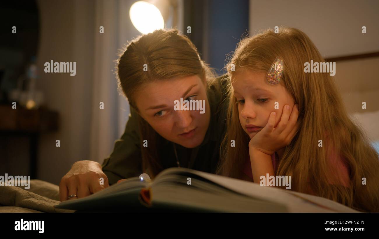 Glückliche kaukasische Familie liebevolle fürsorgliche Mutter liest Buch für kleine Kind Tochter mit Taschenlampe im Schlafzimmer liegen am Abend Mutter und Kind Mädchen Stockfoto