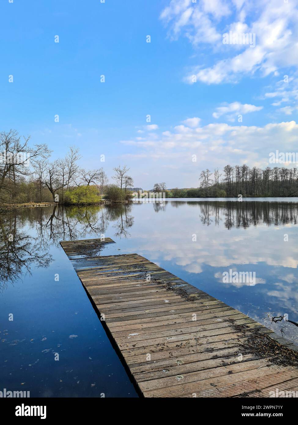 Blick von einem muffigen alten Holzsteg auf einem See mit Sonnenwolken, die sich im Wasser spiegeln, stimmungsvolles Ambiente Stockfoto