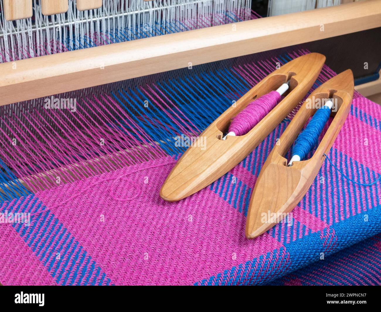 HandWebstuhl und Shuttles mit Gewinde, selektiver Fokus. Kombination aus rosa und blauen Farben. Webkonzept Stockfoto