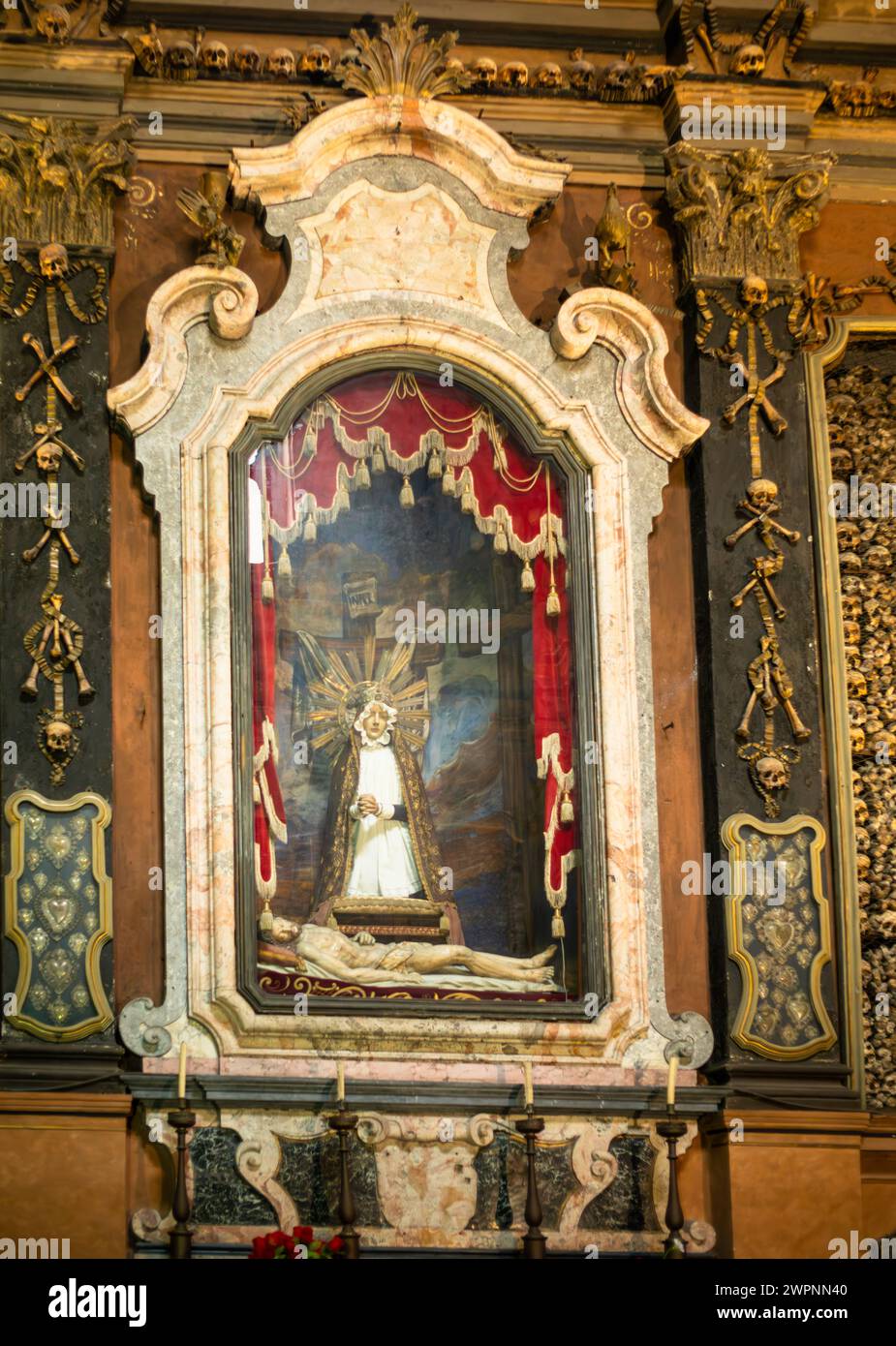 Ein katholischer Schrein zwischen angeordneten Schädeln und Knochen im Ossuar in der Chiesa di San Bernardino alle Ossa, Mailand, Italien Stockfoto