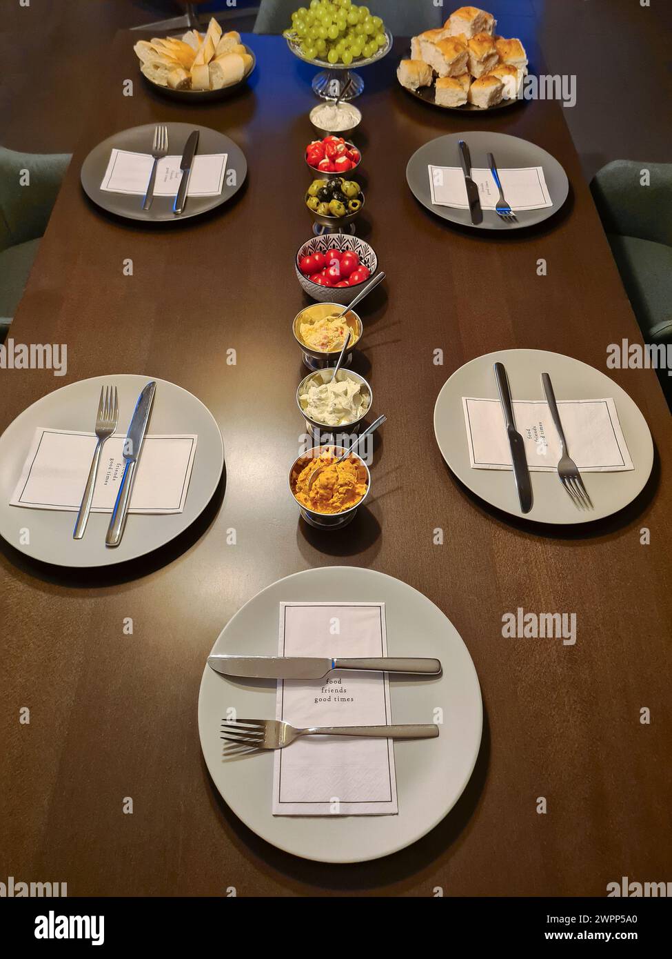 Ein Arrangement von kleinen Schüsseln mit Vorspeisen und fünf grauen Tellern mit Besteck und bedruckten Servietten Stockfoto