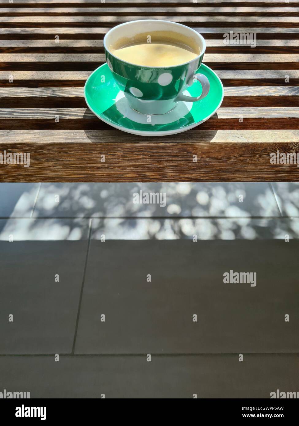 Eine grüne Tasse mit weißen Punkten und frischem Kaffee steht auf einer Holzbank, Kaffeepause Stockfoto