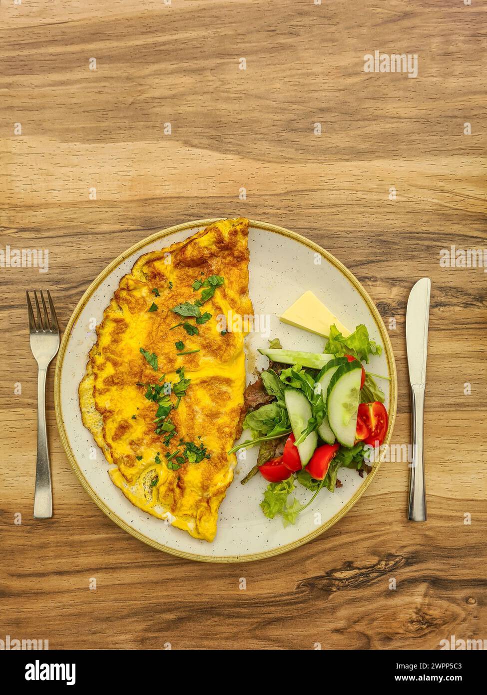 Herzhaftes Omelette mit Petersilie auf einem Teller mit Gurke, Tomatenscheiben, Salat, Butter Stockfoto