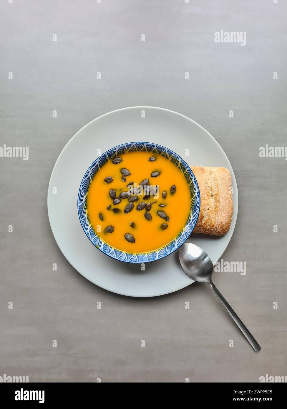 Hausgemachte frische Kürbissuppe garniert mit Kürbiskernen und Leinöl als Topping in einer Suppenschüssel auf einem weißen Teller mit Löffel und Brötchen Stockfoto