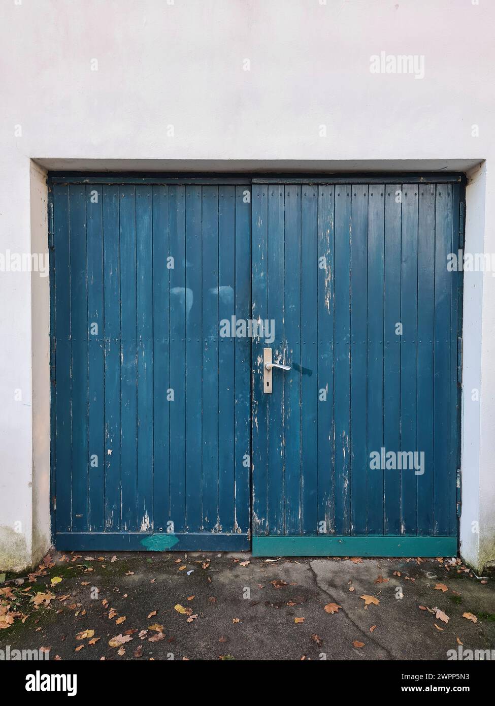 Weiße Wand mit blauem Holztor und Türgriff, Herbstlaub auf dem Boden, Deutschland Stockfoto