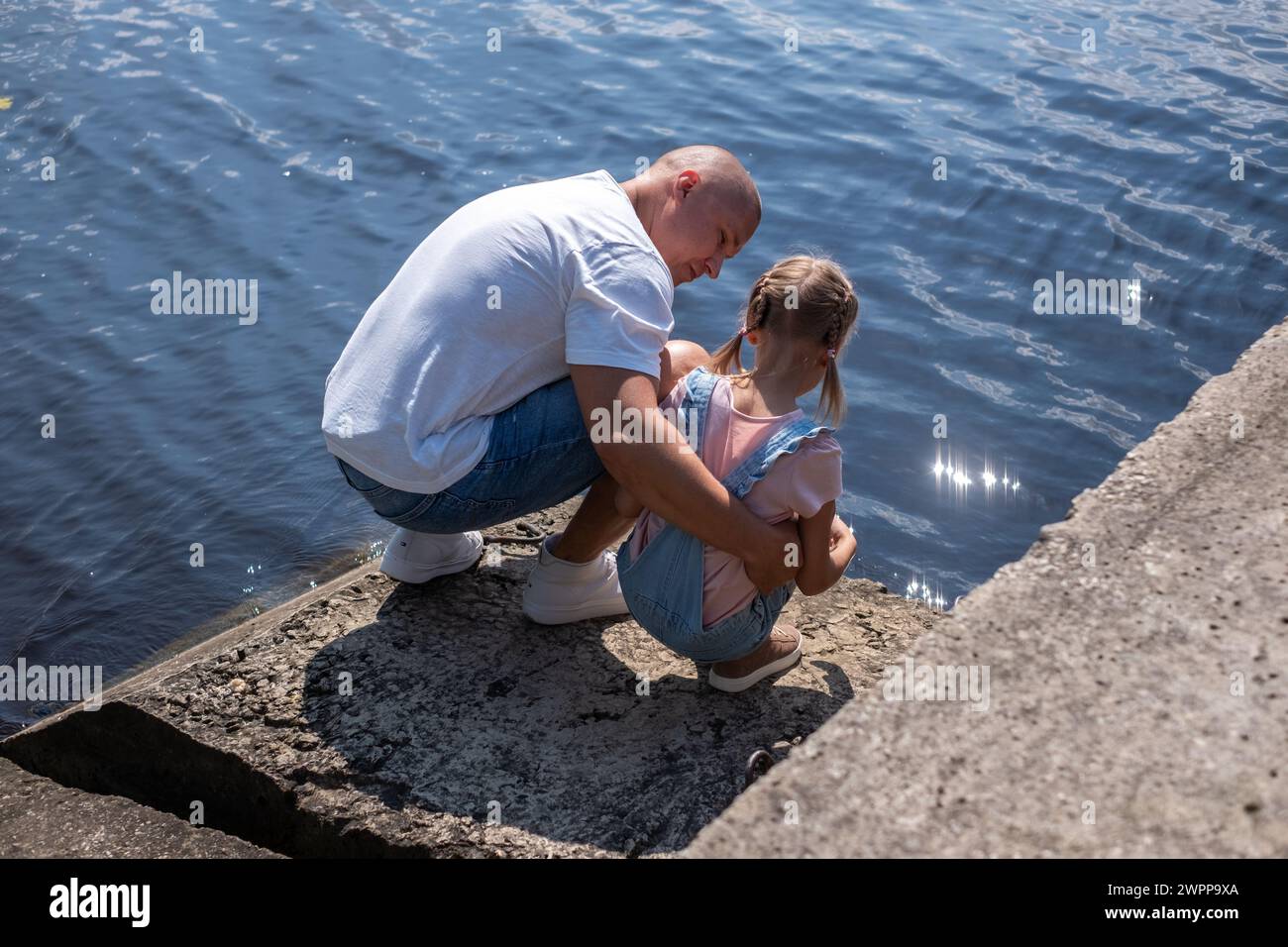 Ein Vater wird von seiner Tochter am Rande des Wassers gehockt, Gespräche werden geteilt. Schlägt Beratung, Pflege und Familienbindungszeit und Krankenversicherung wann vor Stockfoto