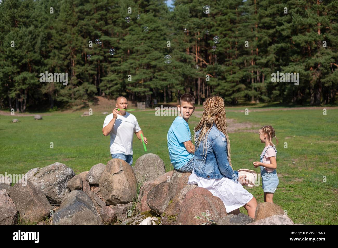 Eine Familie genießt ein Outdoor-Abenteuer in einer Kiefernwaldlichtung, dieses Bild verkörpert den Geist des Kinderspiels und der Familienspaß in der Natur. Stockfoto
