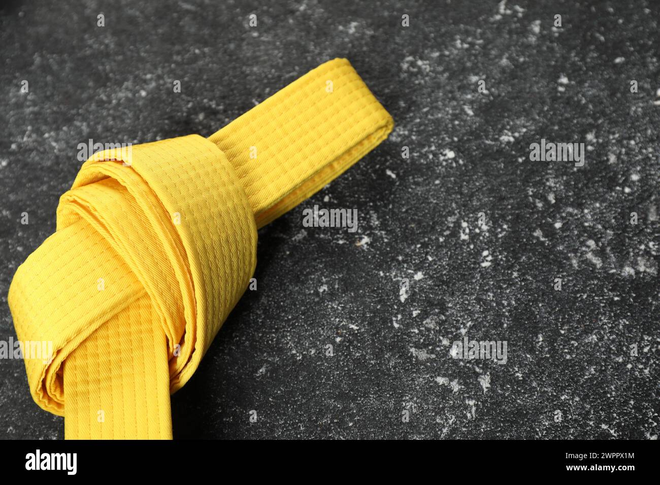 Gelber Karategürtel auf grauem, strukturiertem Hintergrund, Platz für Text Stockfoto