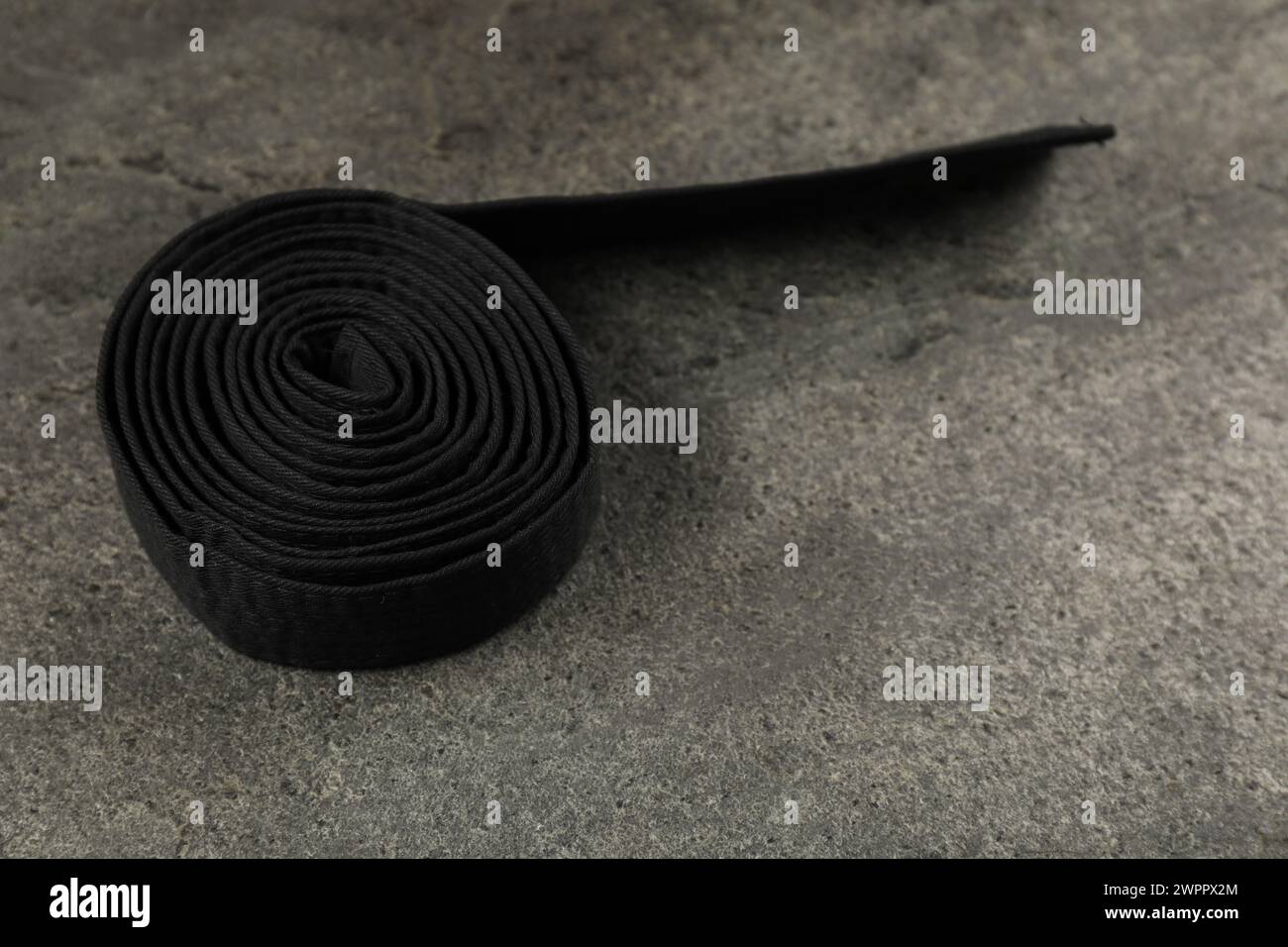Schwarzer Karategürtel auf grauem, strukturiertem Hintergrund, Platz für Text Stockfoto