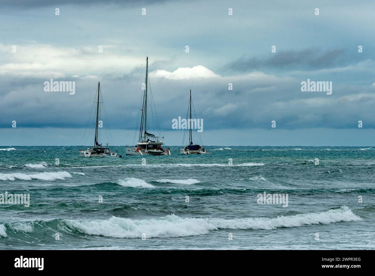 Dramatisches Bild des Karibischen Meeres mit Segelbooten in der Bucht mit stürmischen Wolken und rauen Gewässern und Wellen. Stockfoto