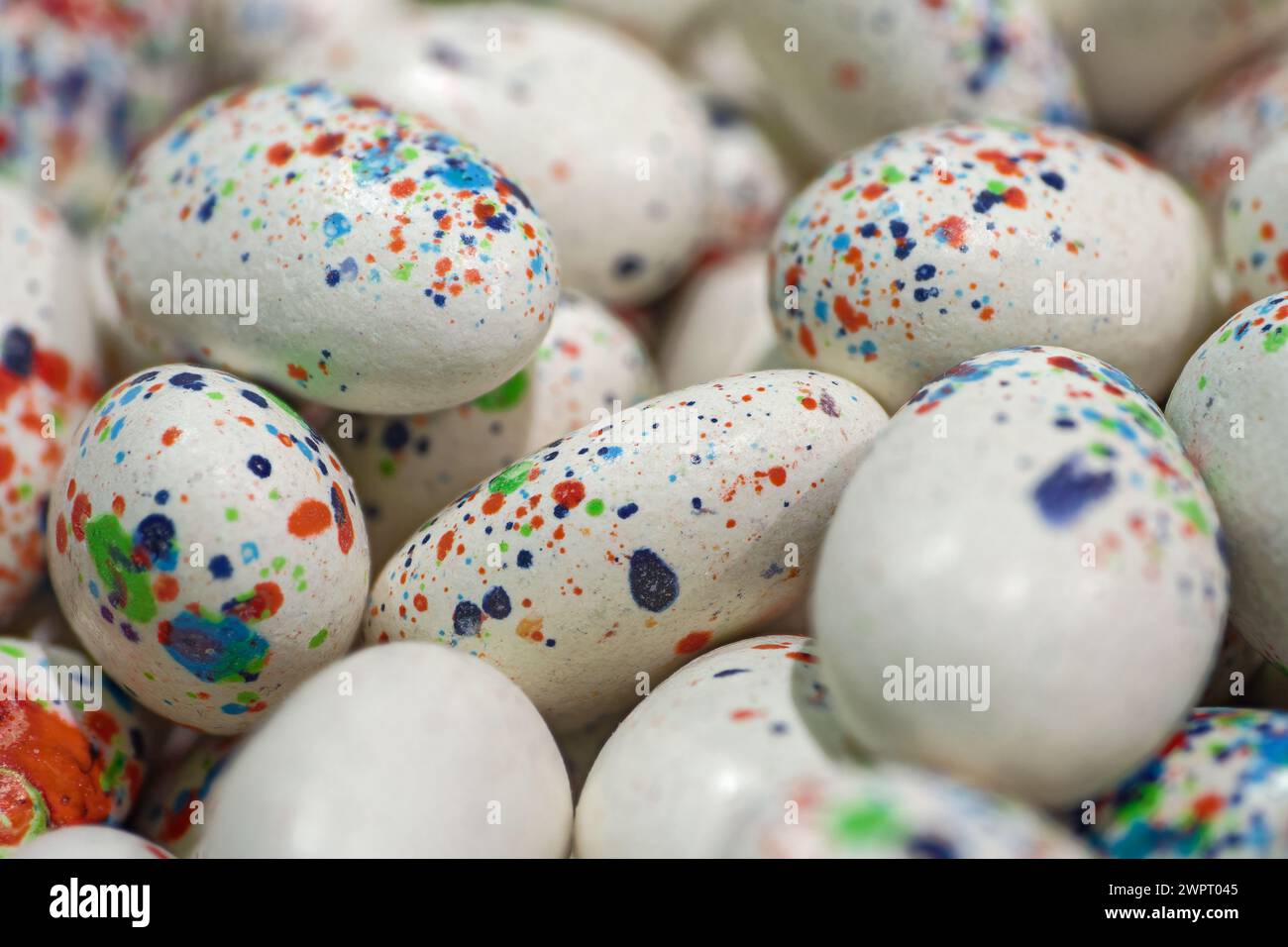 Weiße eiförmige Dragees mit hellen, mehrfarbigen Flecken, Nahaufnahme, abstraktem ostern- oder Süßwarenhintergrund Stockfoto