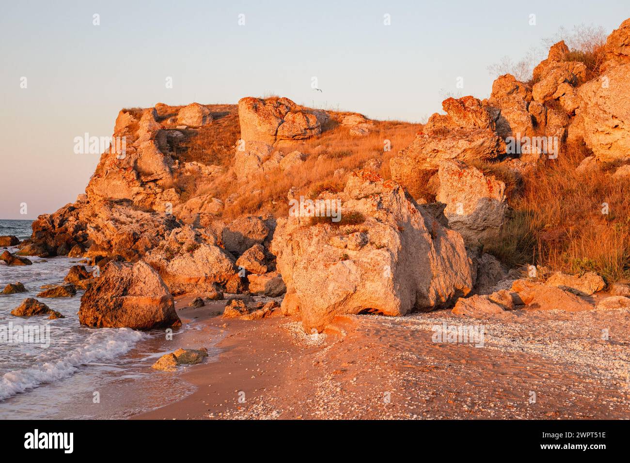 Rote Felsen, beleuchtet von der untergehenden Sonne an der Küste des Asowschen Meeres. Reisen und Tourismus. Stockfoto