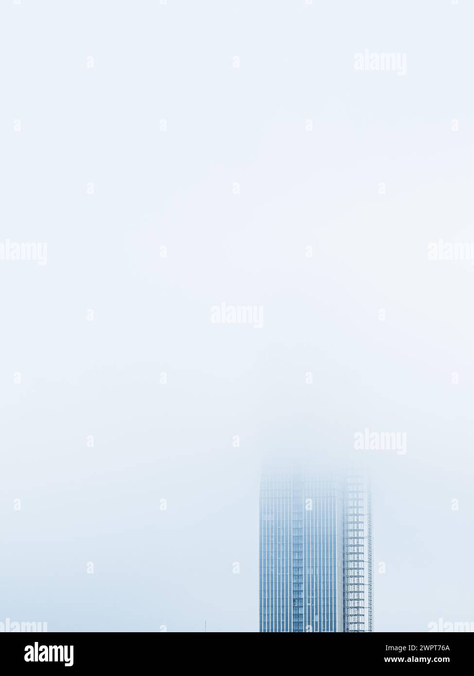 Die Spitze eines hohen Wolkenkratzers erhebt sich aus einem dicken, nebeligen Schleier vor einem ruhigen Himmel in Göteborg, Schweden. Der Morgennebel verdeckt teilweise den Mo Stockfoto
