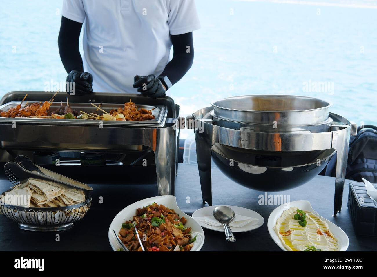 Ein Service-Mitarbeiter auf einer Yacht arrangiert eine Mahlzeit mit einer Auswahl an Gerichten für die Gäste vor dem Hintergrund des Meeres Stockfoto