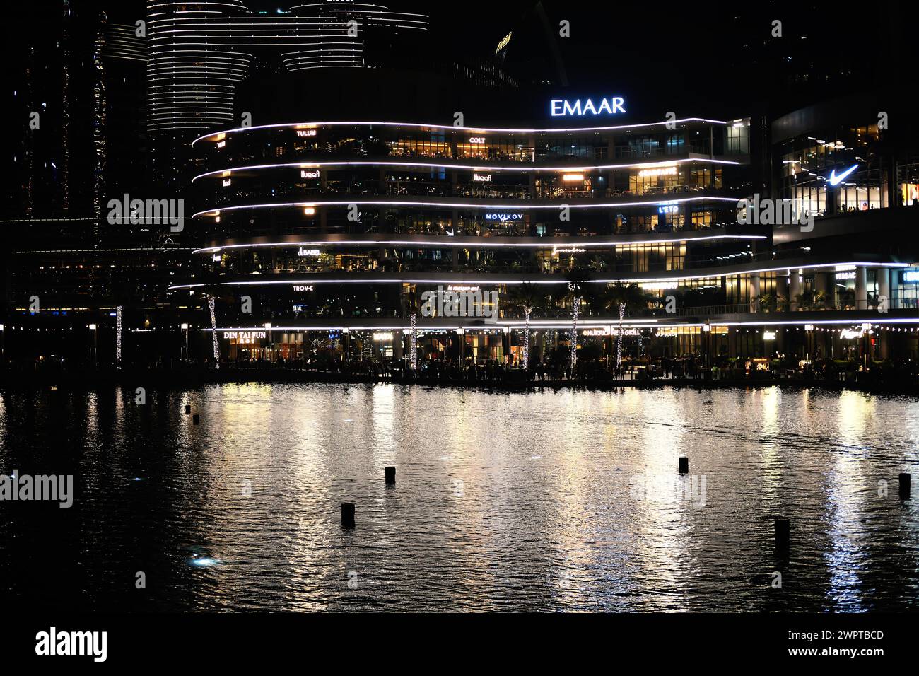 Nächtlicher Blick auf Dubais pulsierende Uferpromenade mit beleuchteten modernen Gebäuden, die sich auf der ruhigen Wasseroberfläche spiegeln. Dubai, VAE - 15. August 2023 Stockfoto