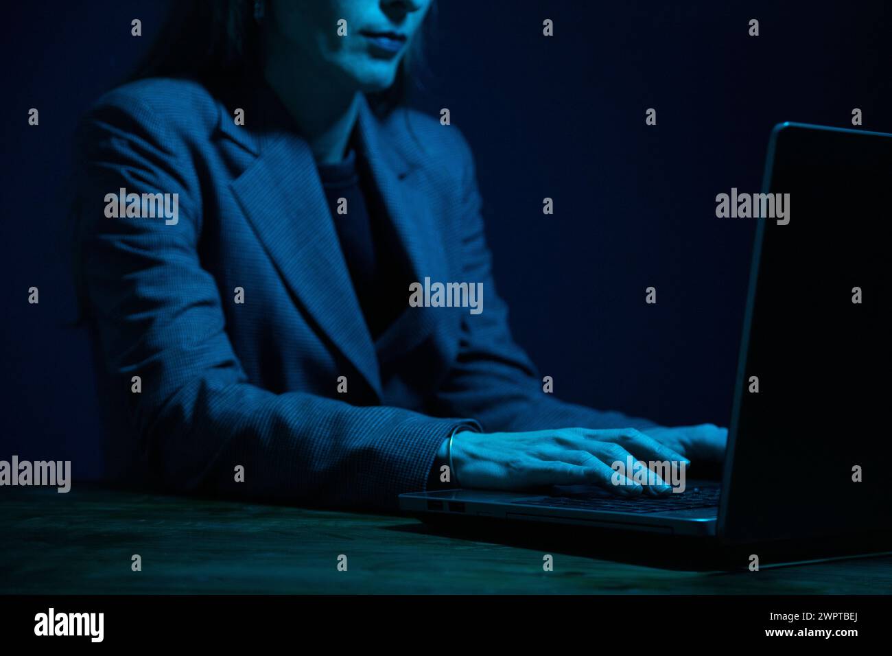 Geschäftsfrau, die im Dunkeln an einem Laptop arbeitet und vom Bildschirm beleuchtet wird. Keine Fläche. Konzentrieren Sie sich auf die Hände. Blaue Farbkorrektur Stockfoto