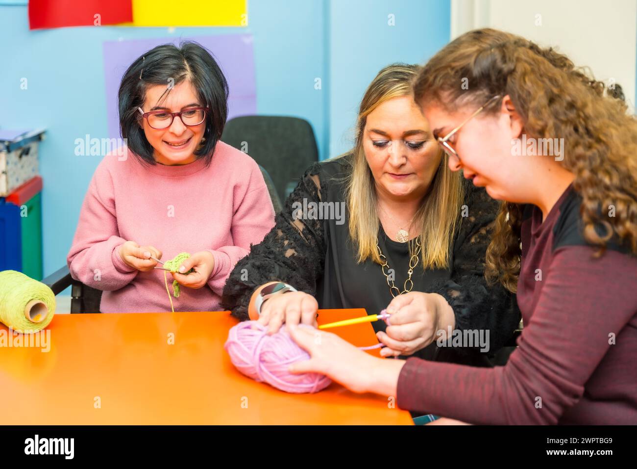 Frauen mit geistiger Behinderung und Lehrerin, die das Stricken von Kleidung mit Wolle lernt Stockfoto