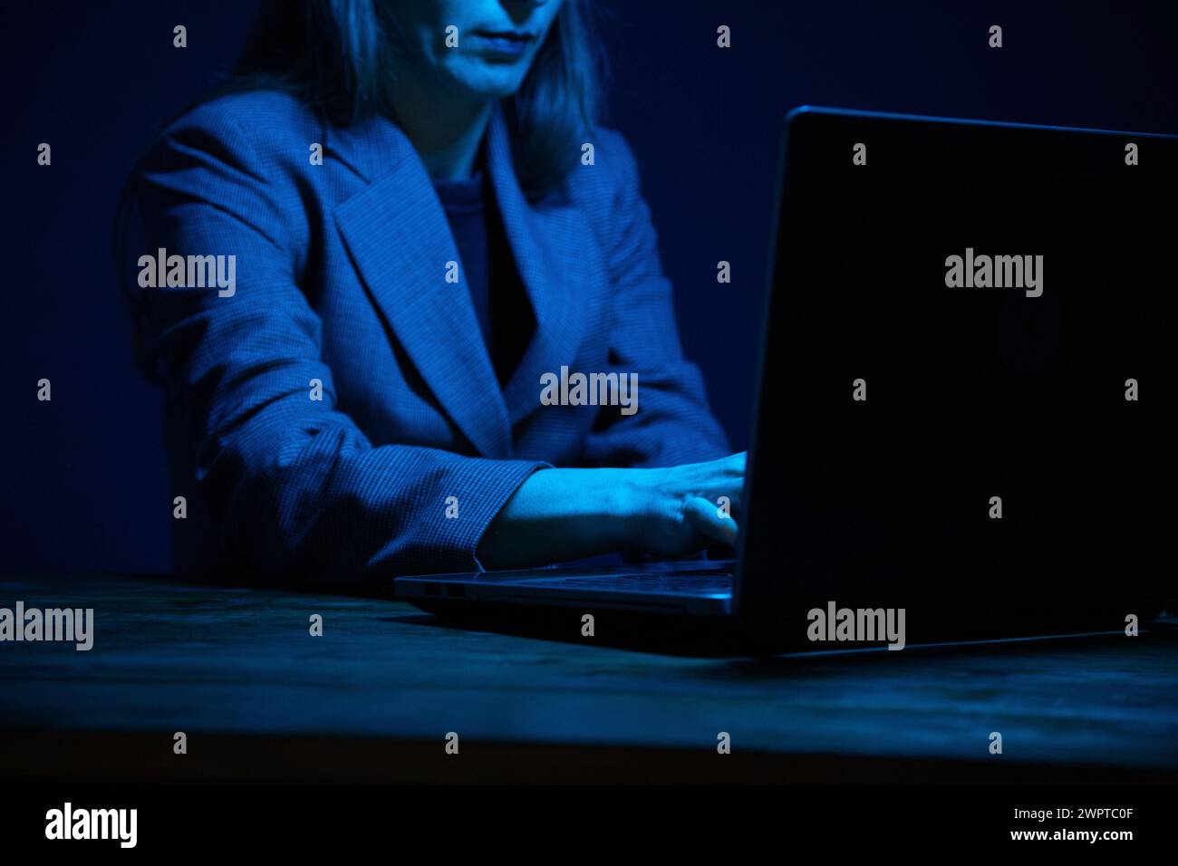 Geschäftsfrau, die im Dunkeln an einem Laptop arbeitet und vom Bildschirm beleuchtet wird. Keine Fläche. Konzentrieren Sie sich auf die Hände. Graufarbkorrektur. Stockfoto
