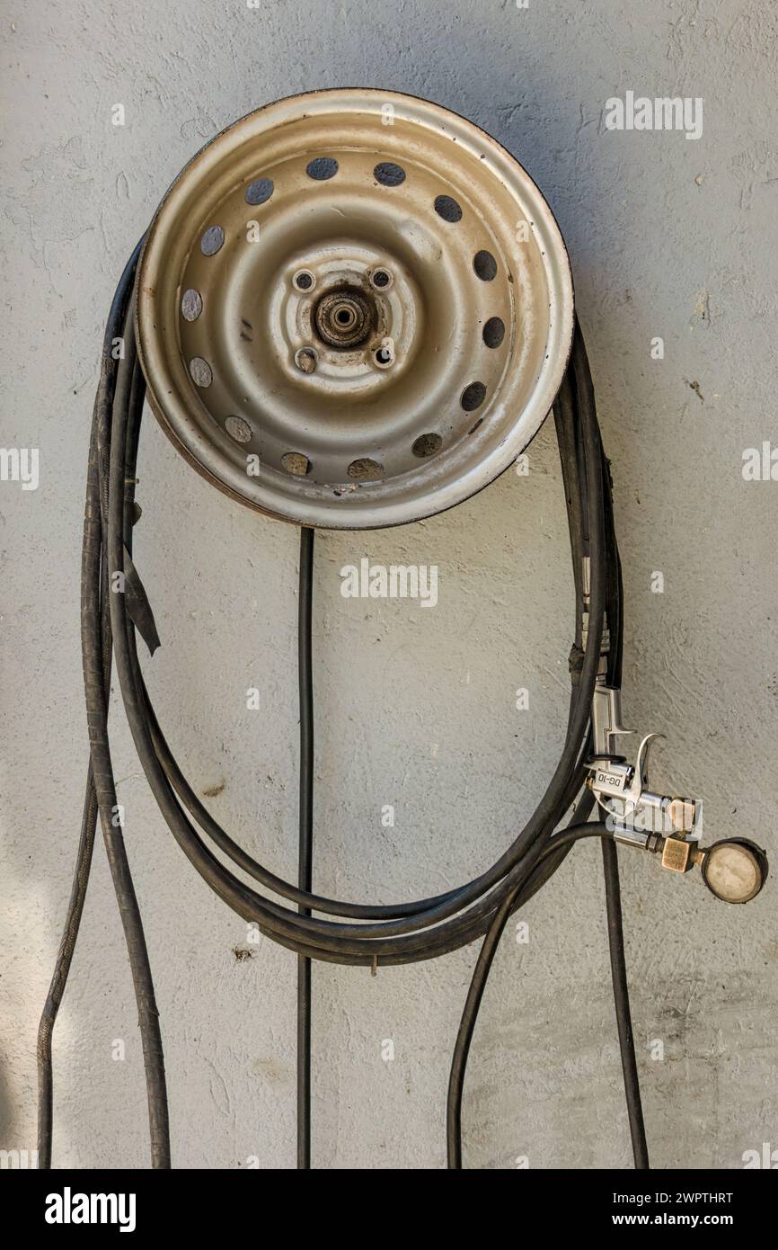 Ein Luftschlauch mit einem kaputten Manometer, der an einem verrosteten Rad hängt, in einer Autowerkstatt in Arcabuco in Zentral-Kolumbien. Stockfoto