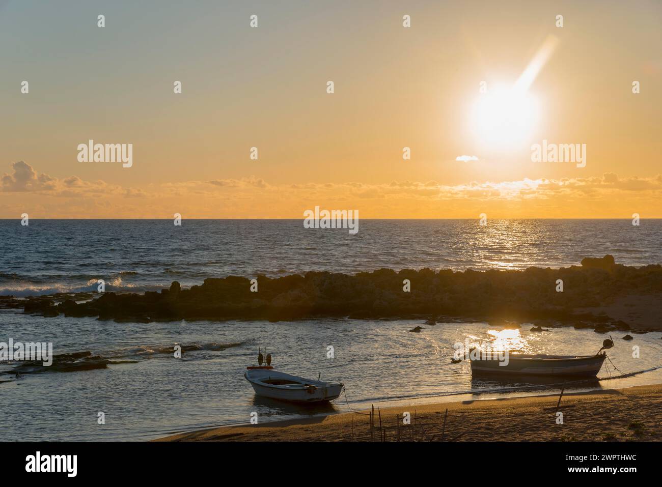 Ein friedlicher Sonnenuntergang am Meer mit Booten und Felsen im goldenen Licht der Abendsonne, Finikounda, Pylos-Nestor, Messinia, Peloponnes, Griechenland Stockfoto