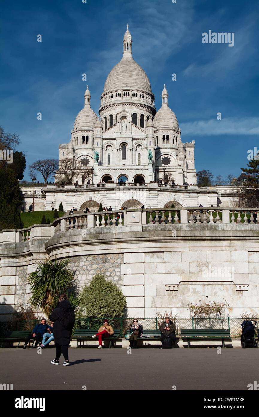 Blick auf die Kuppeln und Türme der Südfassade der Basilika du Sacre Coeur de Montmartre vom Platz Louise Michel aus, wo Leute sitzen Stockfoto