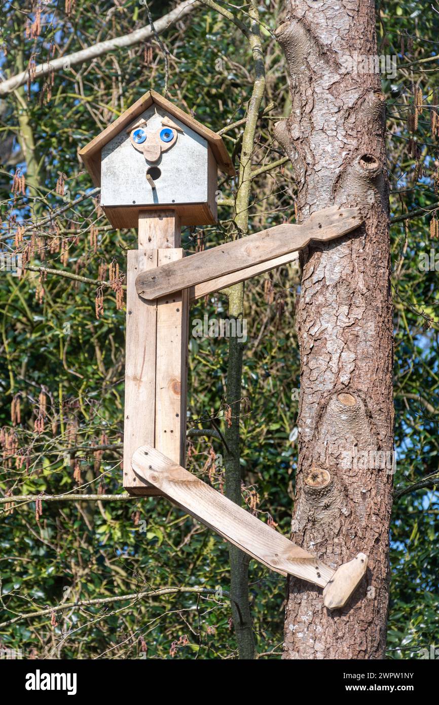 Schrulliger Nestkasten, neuartiger Vogelkasten in Form einer Person, die auf einen Baum klettert Stockfoto