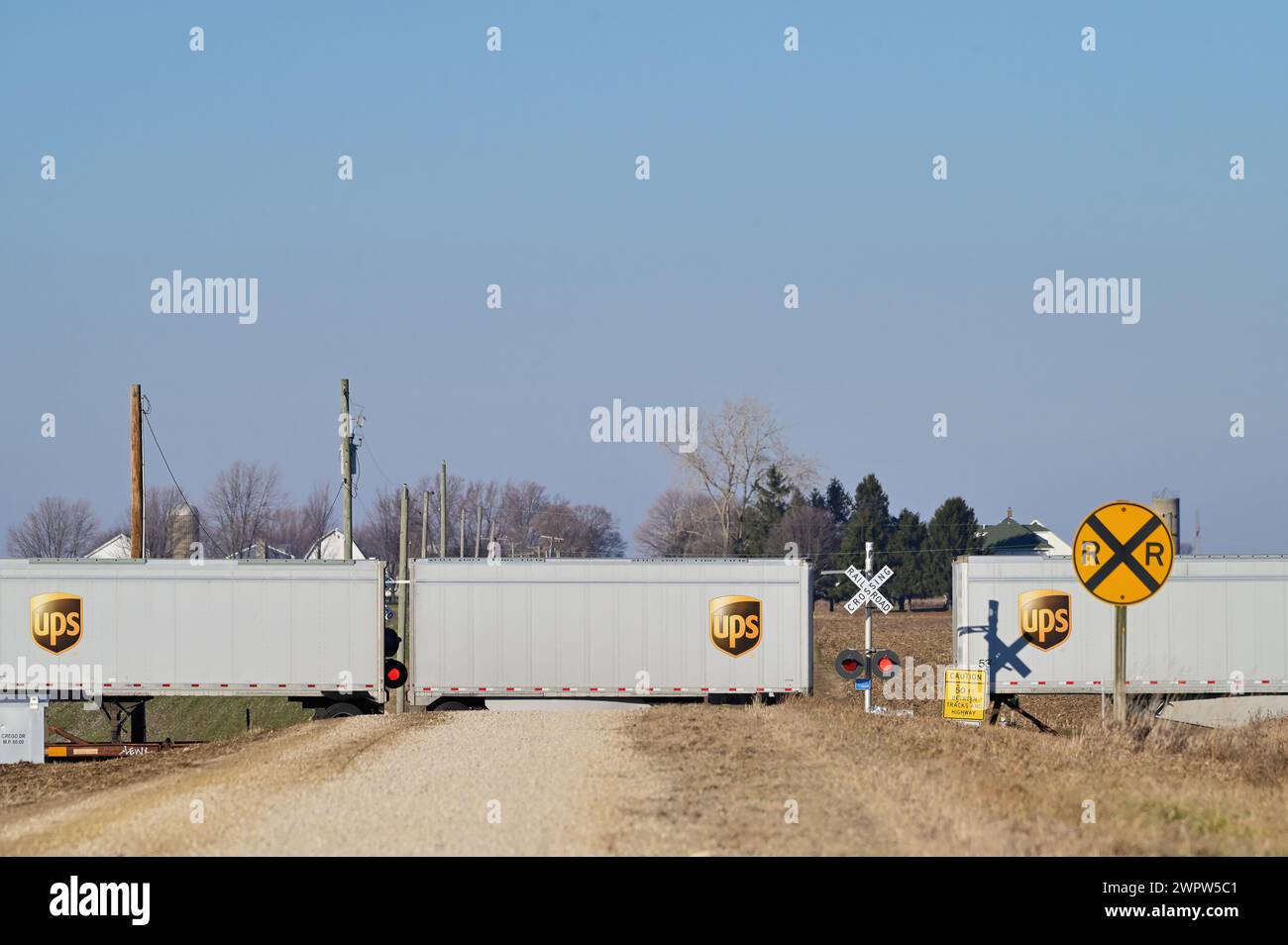 Waterman, Illinois, USA. Ein intermodaler Güterzug brüllt durch einen unbefestigten Straßenübergang, während er westwärts durch das ländliche Illinois fährt. Stockfoto