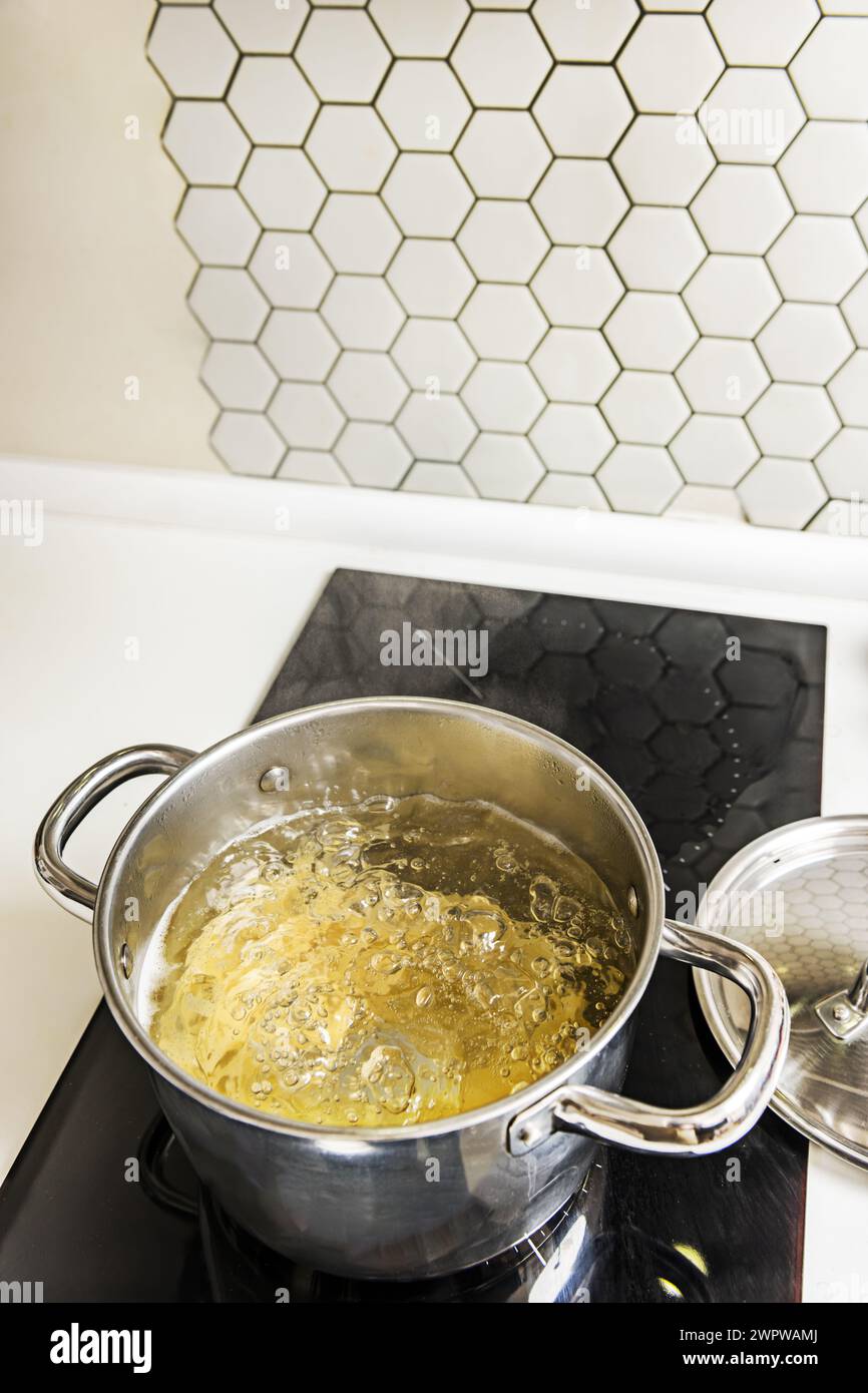 Ein mit kochendem Wasser gefüllter Edelstahltopf zum Kochen von al dente Pasta auf einem Keramikkochfeld mit zwei Kochstellen Stockfoto