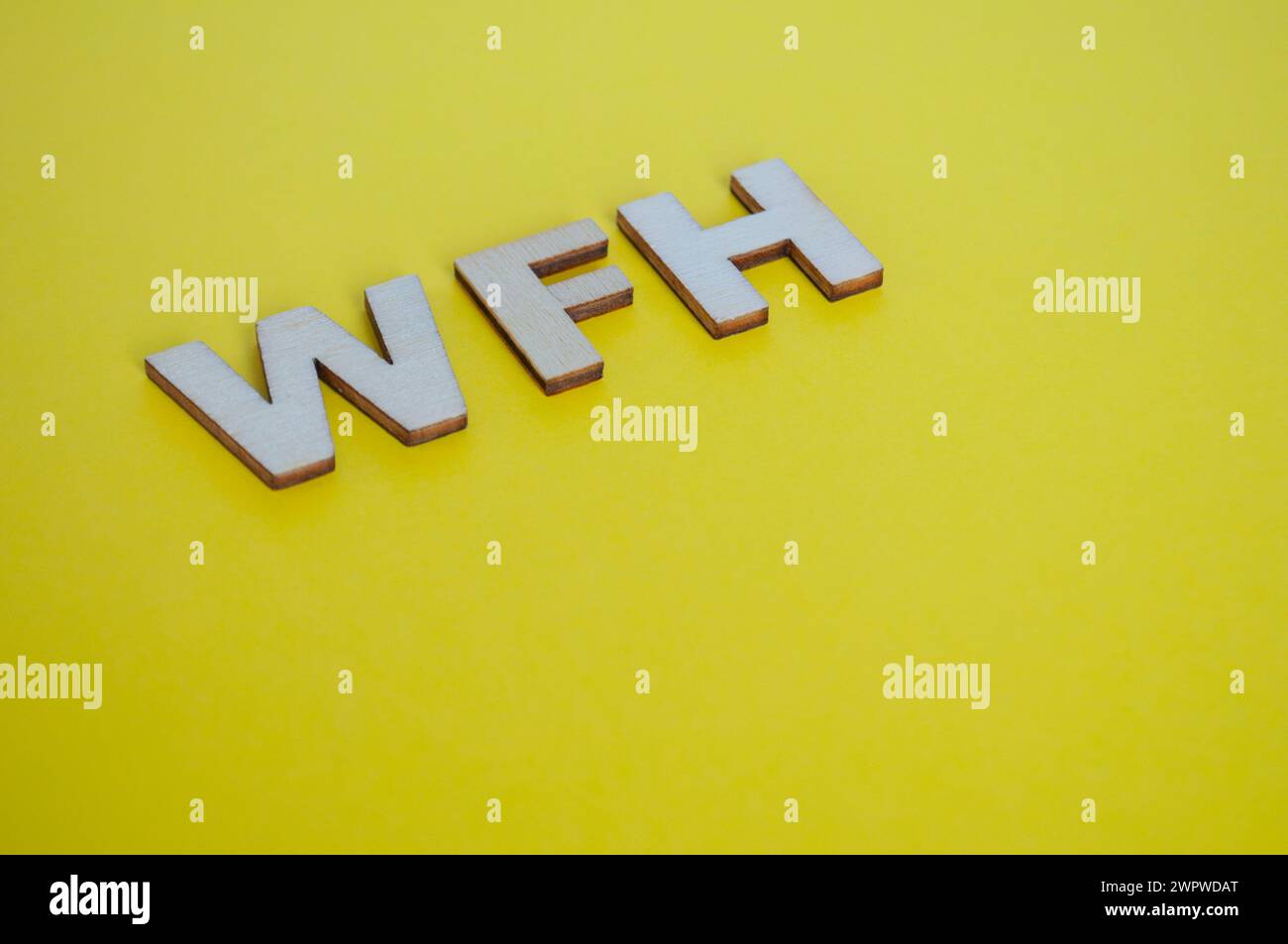 WFH Holzbuchstaben, die Arbeit von Zuhause auf gelbem Hintergrund darstellen. Stockfoto