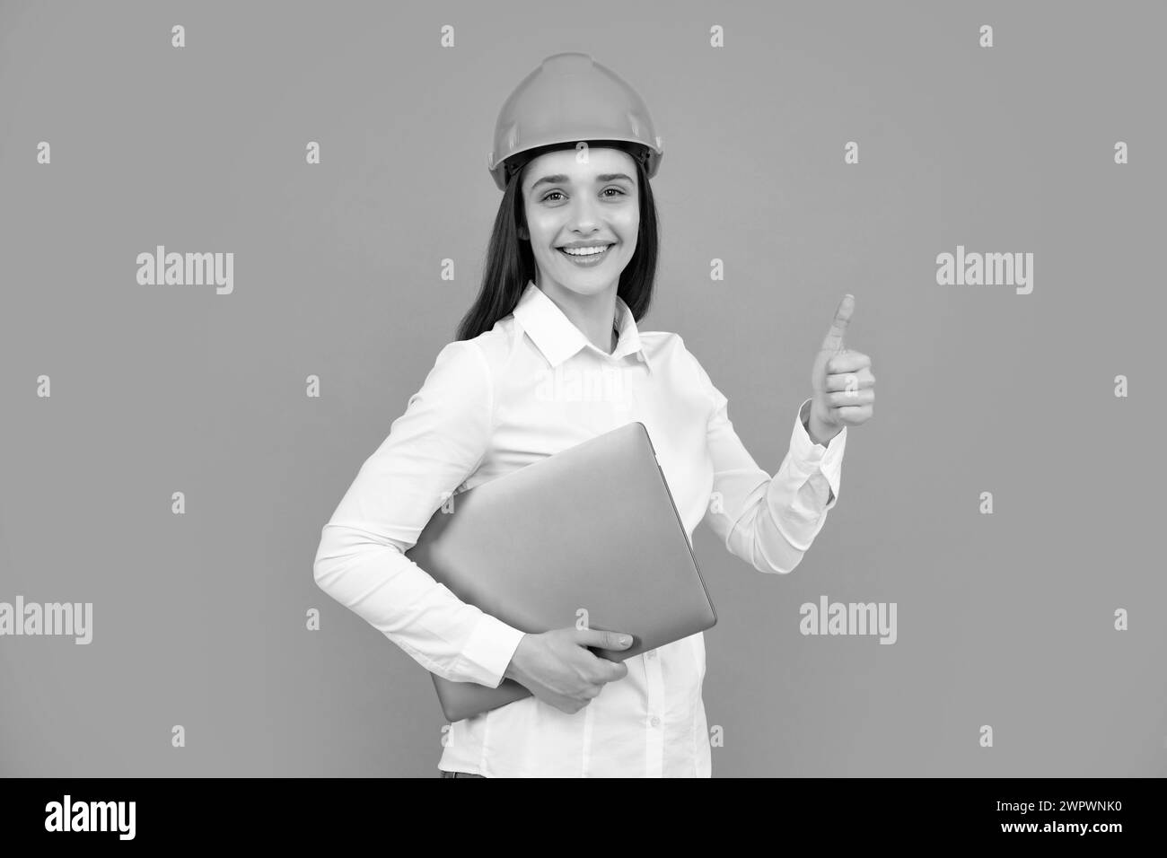 Junge Frau im Helm halten Laptop-Computer auf grauem Hintergrund. Architektin Geschäftsfrau in Helm denken, junge kaukasische Frau in der Arbeit als Stockfoto