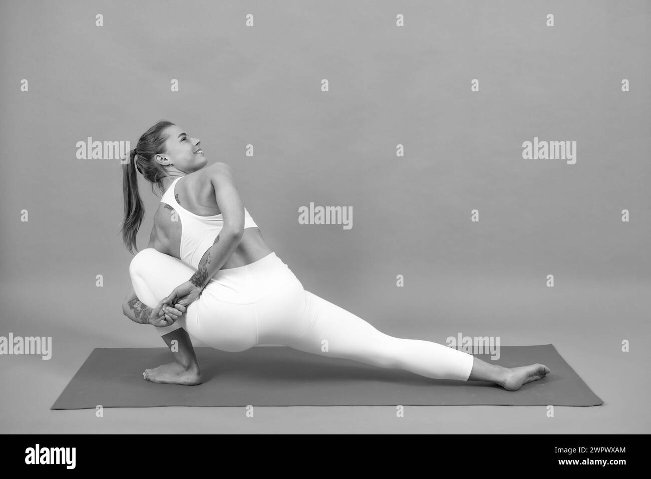 Das sportliche Mädchen hebt während der Übungen auf einer Yogamatte ihre Beine nach oben, grauer Hintergrund mit viel Platz. Stockfoto