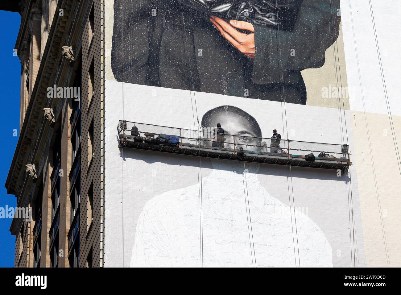 Kommerzielle Künstler, Maler auf einem Hängegerüst, die eine Plakatwerbung an der Seite eines Hochhauses in New York City malen. Stockfoto