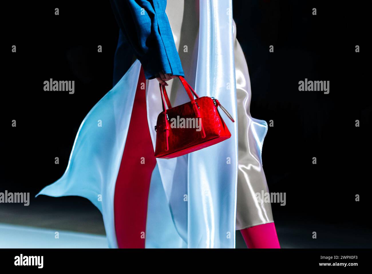 Modische Details eines weißen Seidenkleides und einer roten Handtasche in der Hand einer Frau. Elegante Kleidung und Accessoires Stockfoto