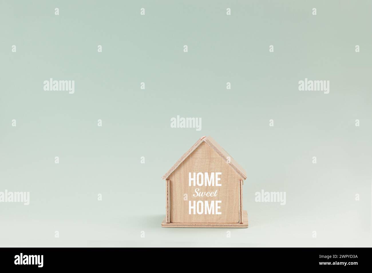 Vereinfachtes hölzernes Hausmodell isoliert auf blassgrünem Hintergrund, mit Text Home Sweet Home on Wall Stockfoto