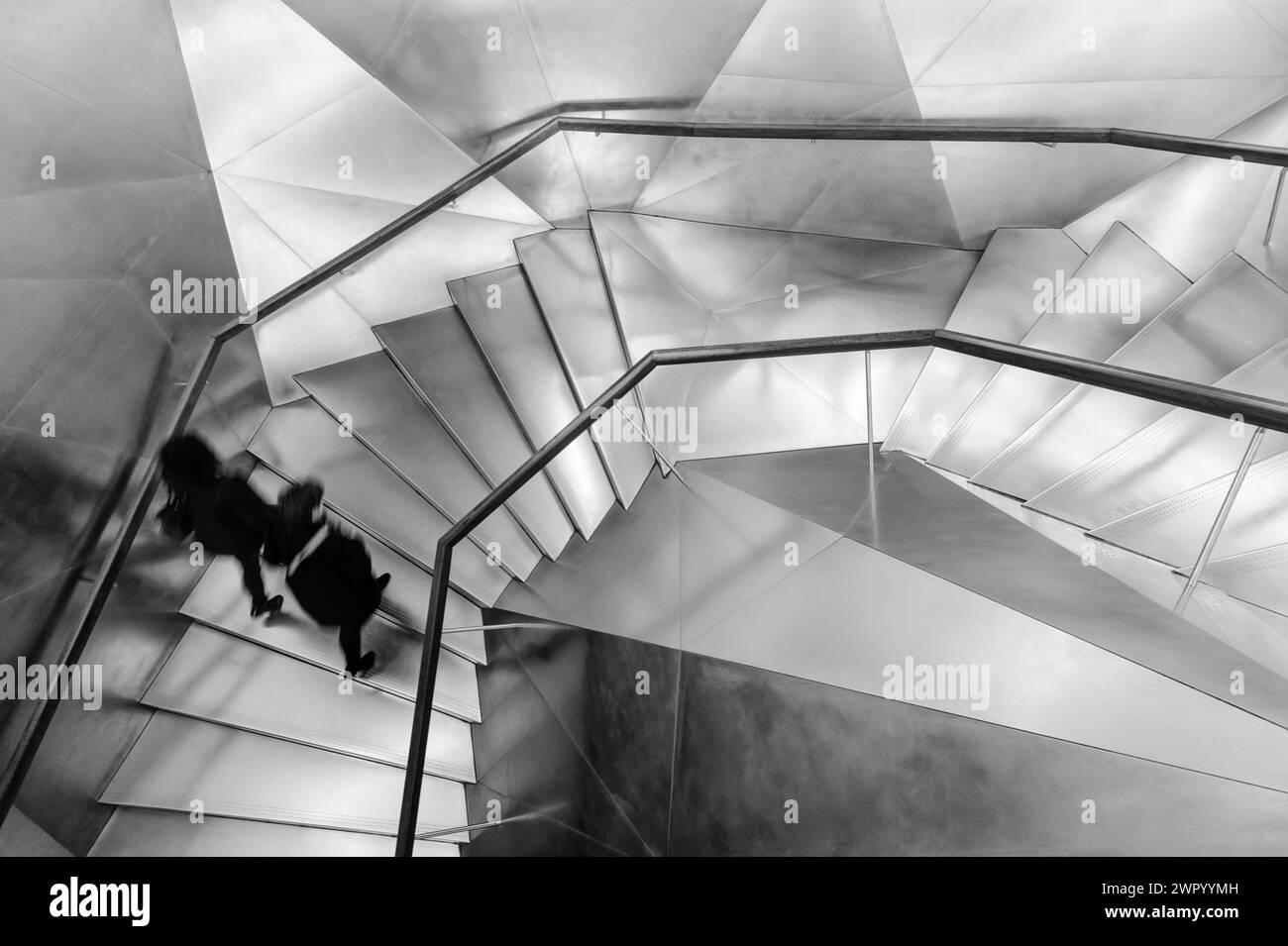 Schwarzweiß-Fotografie der modernen Aluminiumtreppen mit Menschen, die im CaixaForum Museum in Madrid, Spanien, spazieren gehen. Stockfoto