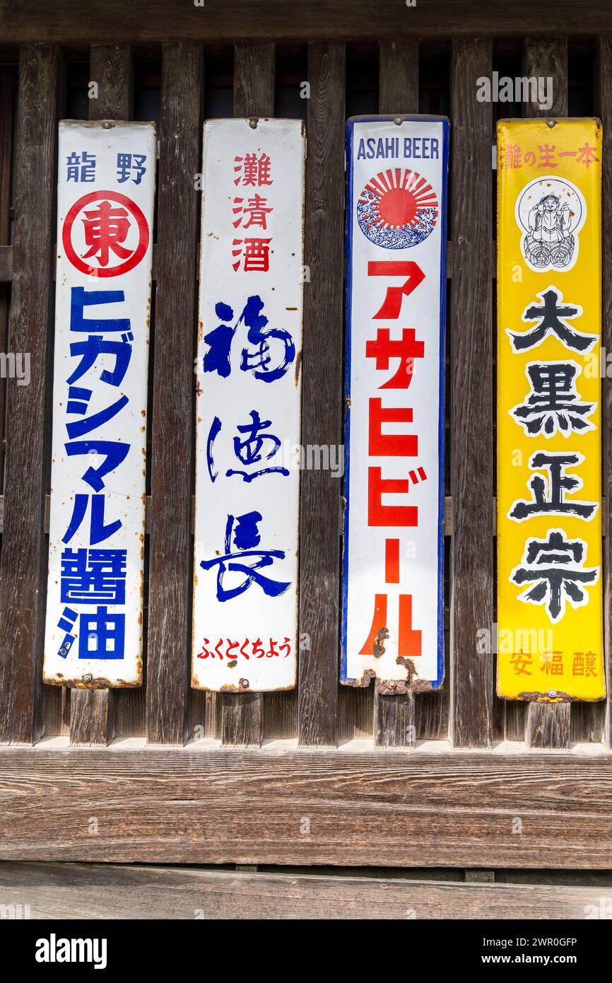 Vier alte, rostende, schmale Metallschilder, die für verschiedene Marken von japanischem Bier werben, die an einen Fensterrahmen aus Holz mit Lattenrost in Tatsuno, Japan, genagelt wurden. Stockfoto