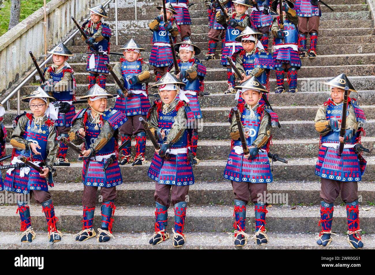 Japanische Kinder, die als Teppou-Aschigaru-Soldaten gekleidet sind, stehen auf Steintreppen und feuern ihre Streichholzpistolen während der Samurai-Parade in Tatsuno ab Stockfoto