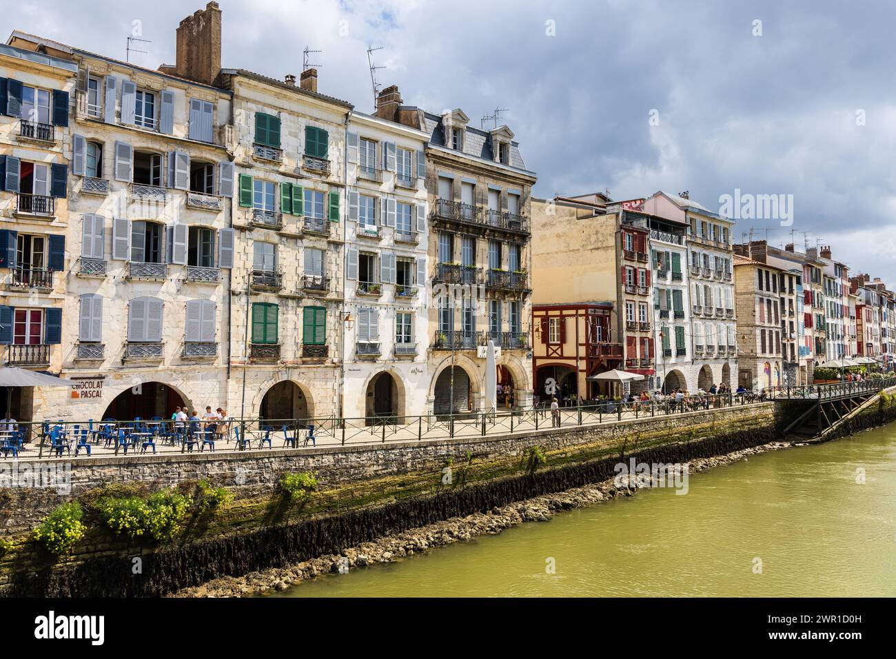 Ein Blick auf traditionelle alte französische Häuser mit bunten Fensterläden, den Fluss Nive und seinen Damm. Bayonne, Pyrénées-Atlantiques, Frankreich. Stockfoto