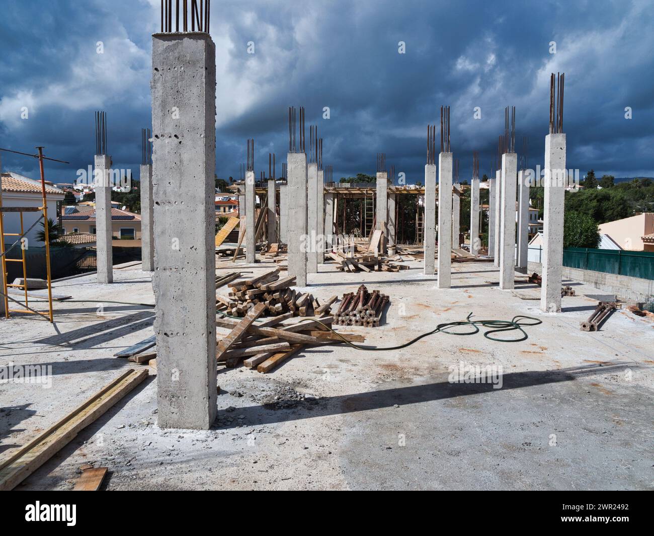 Baustelle: Ein neues Zuhause bauen. Skelettgerüst in Form von zahlreichen Säulen, Eisenverstärkungen, Zementstapeln, Holz... Stockfoto