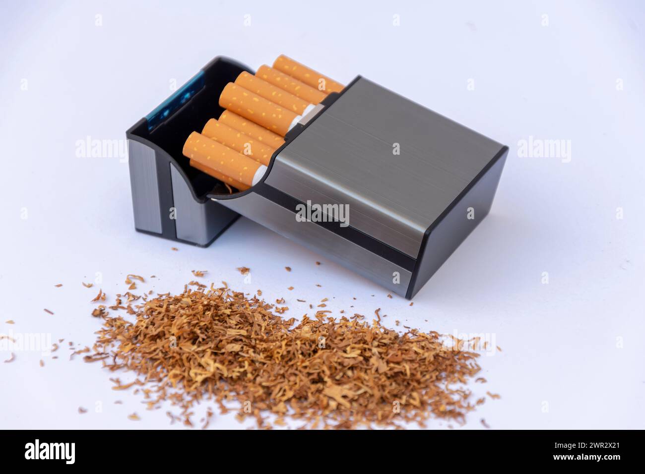 Eine Plastikkiste neben einem Stapel verstreuten Tabaks auf weißem Hintergrund. Stockfoto