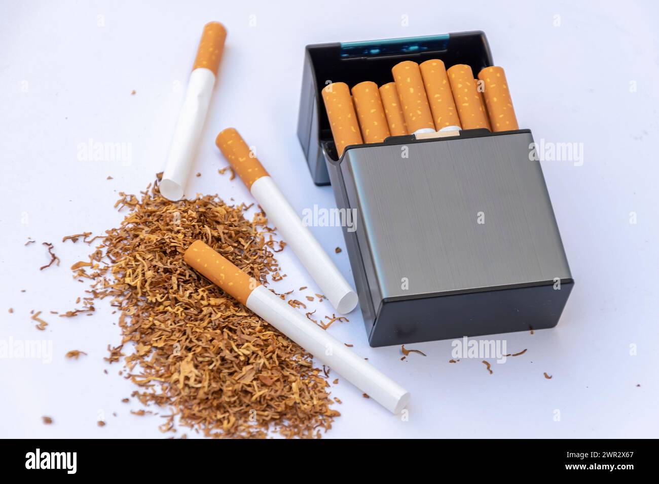 Zigarettenetui neben verstreutem Rauchtabak und leeren Zigarettenhüllen auf weißem Hintergrund. Stockfoto