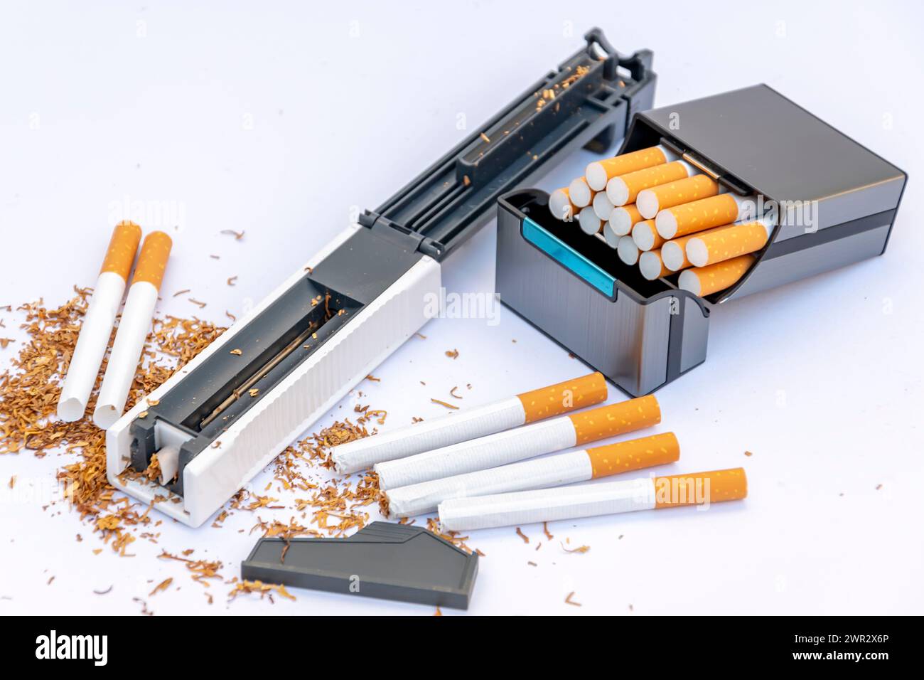 Füllmaschine für mit Tabak gefüllte Zigarettenhüllen, leere Zigaretten auf weißem Hintergrund, Zigarettenetui mit selbstgemachten Zigaretten. Stockfoto