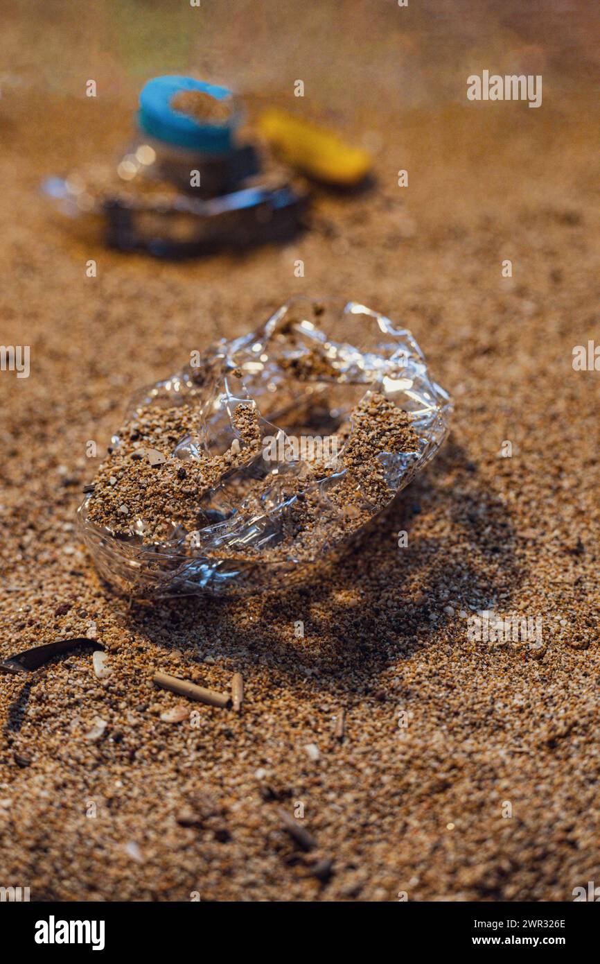 Verlassener Plastikmüll am Strand, im Vordergrund gebrochene Flasche, vertikales Bild Stockfoto