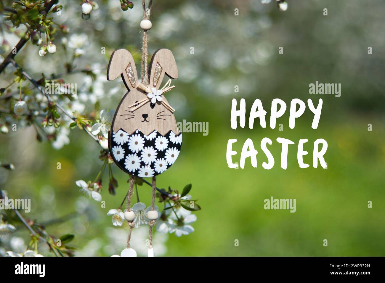 Grußkarte mit Text Happy Easter auf Englisch. Osterdekor. Dekoratives hölzernes Osterhasen-Spielzeug auf dem Hintergrund des blühenden Frühlingsgartens. Im Freien Stockfoto