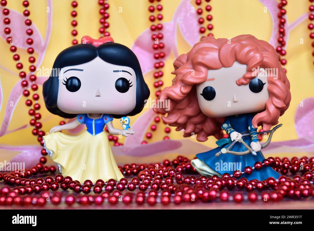 Funko Pop Actionfiguren der Disney Prinzessinnen Schneewittchen und Merida (tapfer). Goldener rosa Vorhang, rote Halskette, fabelhafter Palast. Stockfoto